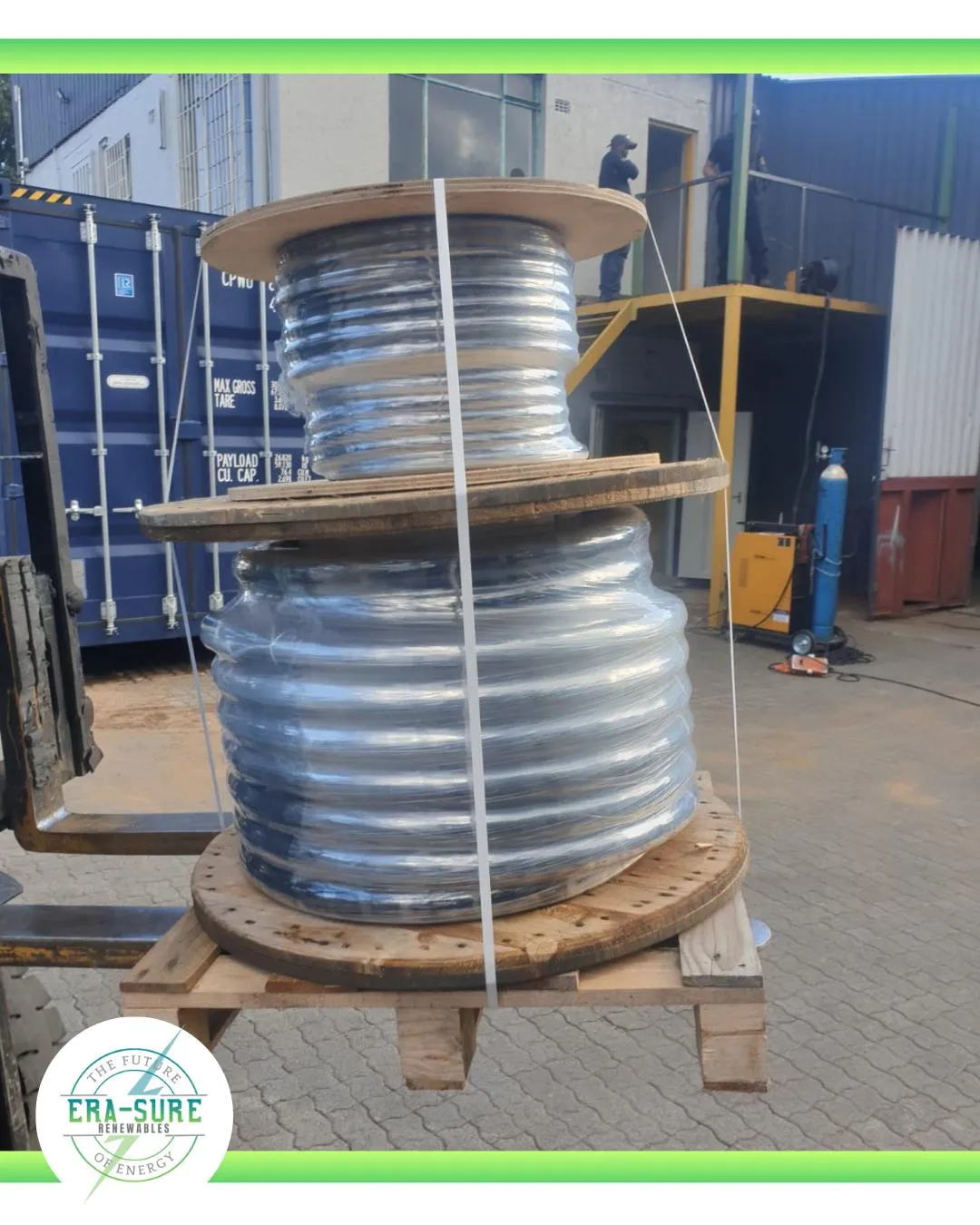 A drum of clear-sheathed armoured cable strapped to a pallet in a yard.
