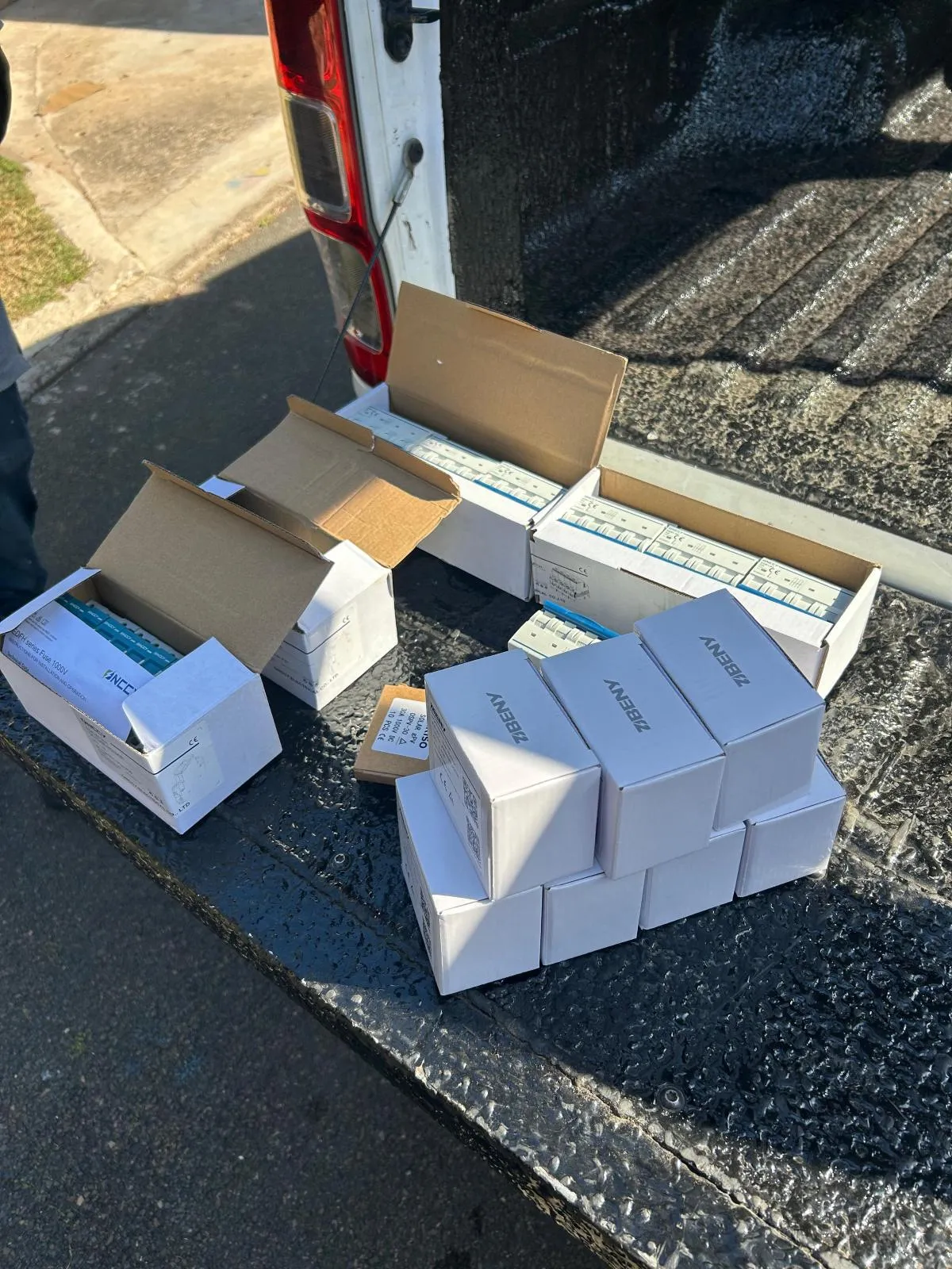 Open cartons of modular circuit breakers and fuse holders with smaller boxed components on a vehicle tailgate