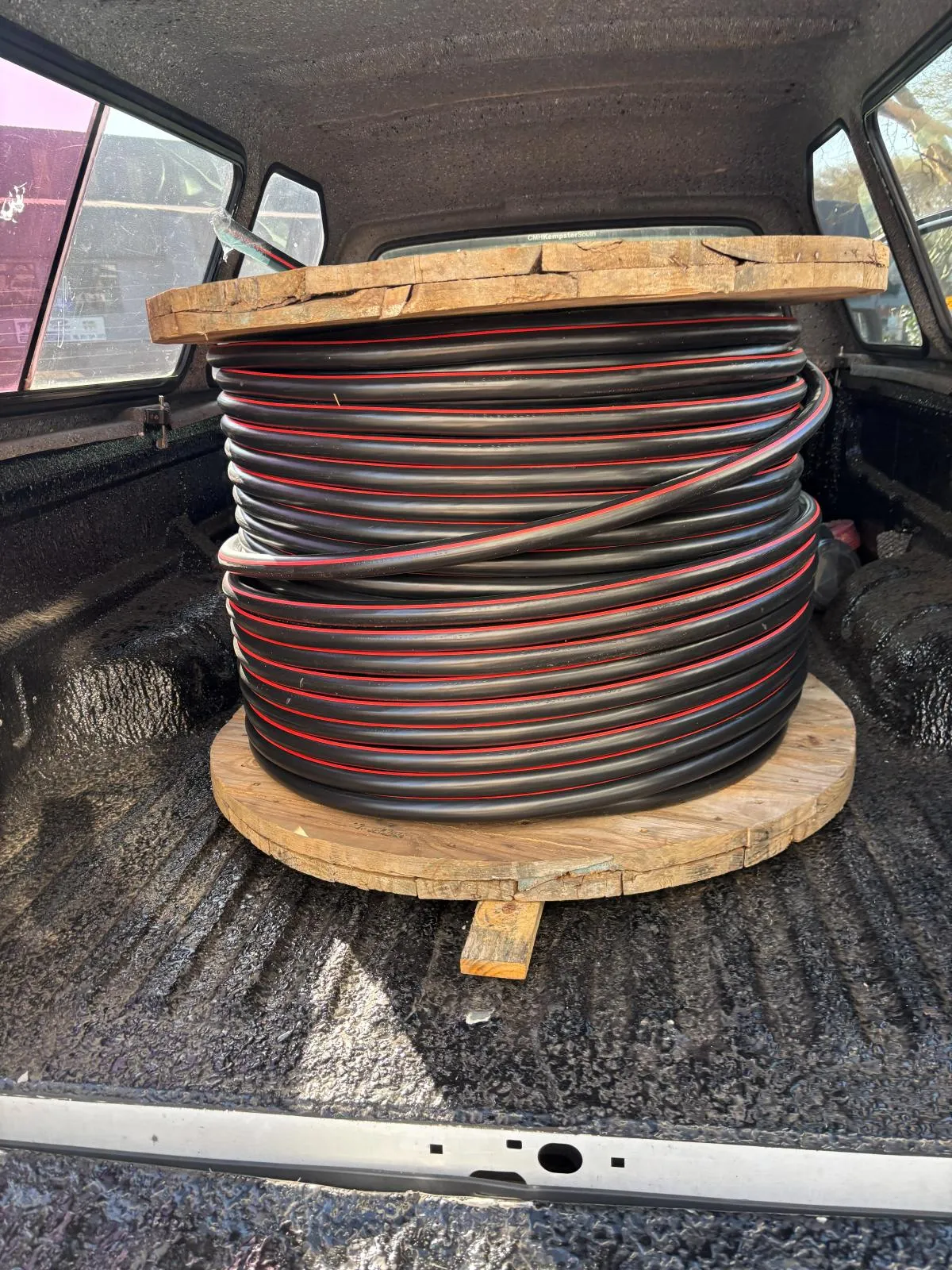 A drum of red, black and grey cable secured in a vehicle load bed.