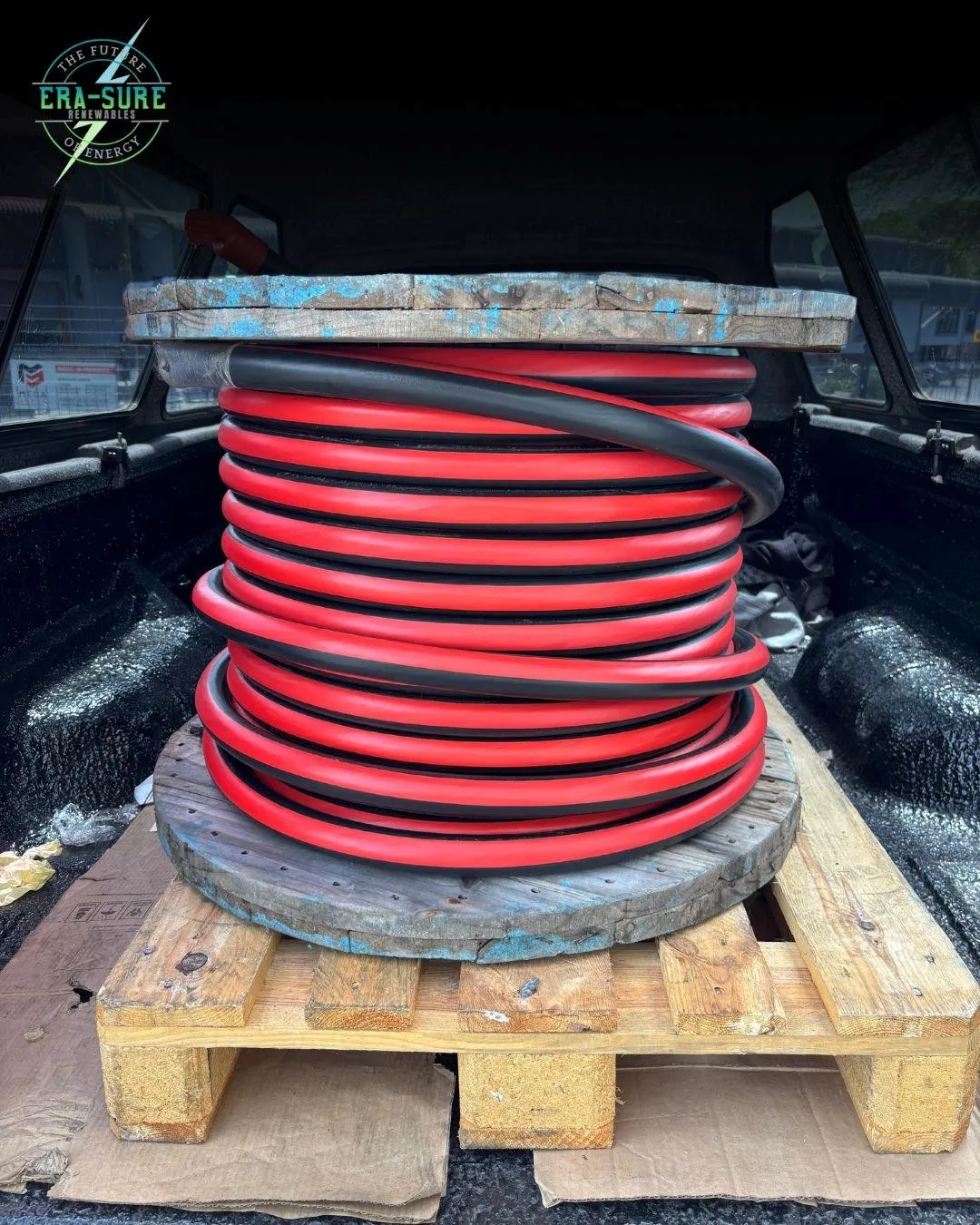 Coiled red and black cable on a drum, palletised in a vehicle load bed.