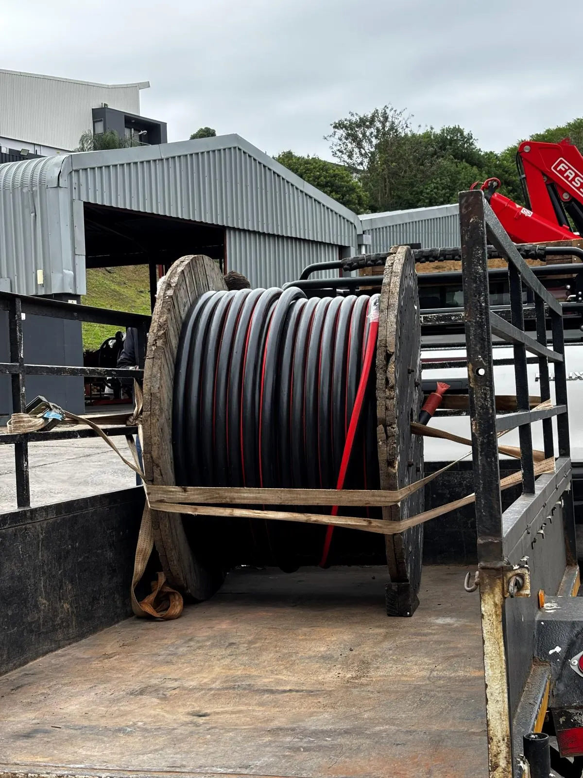 A large cable drum secured on a truck-mounted crane bed for transport.