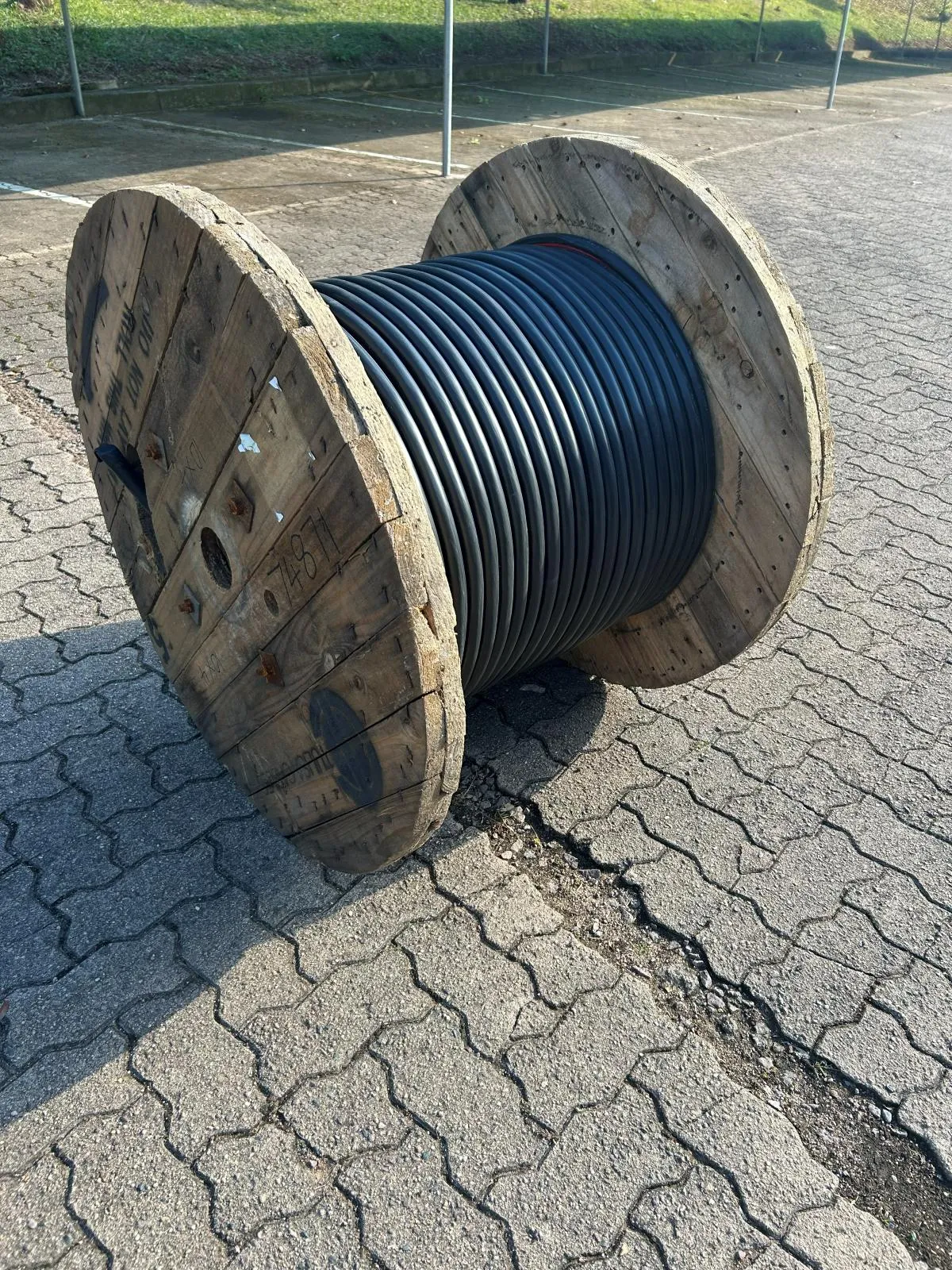 A wooden drum wound with heavy black cable standing on paving.