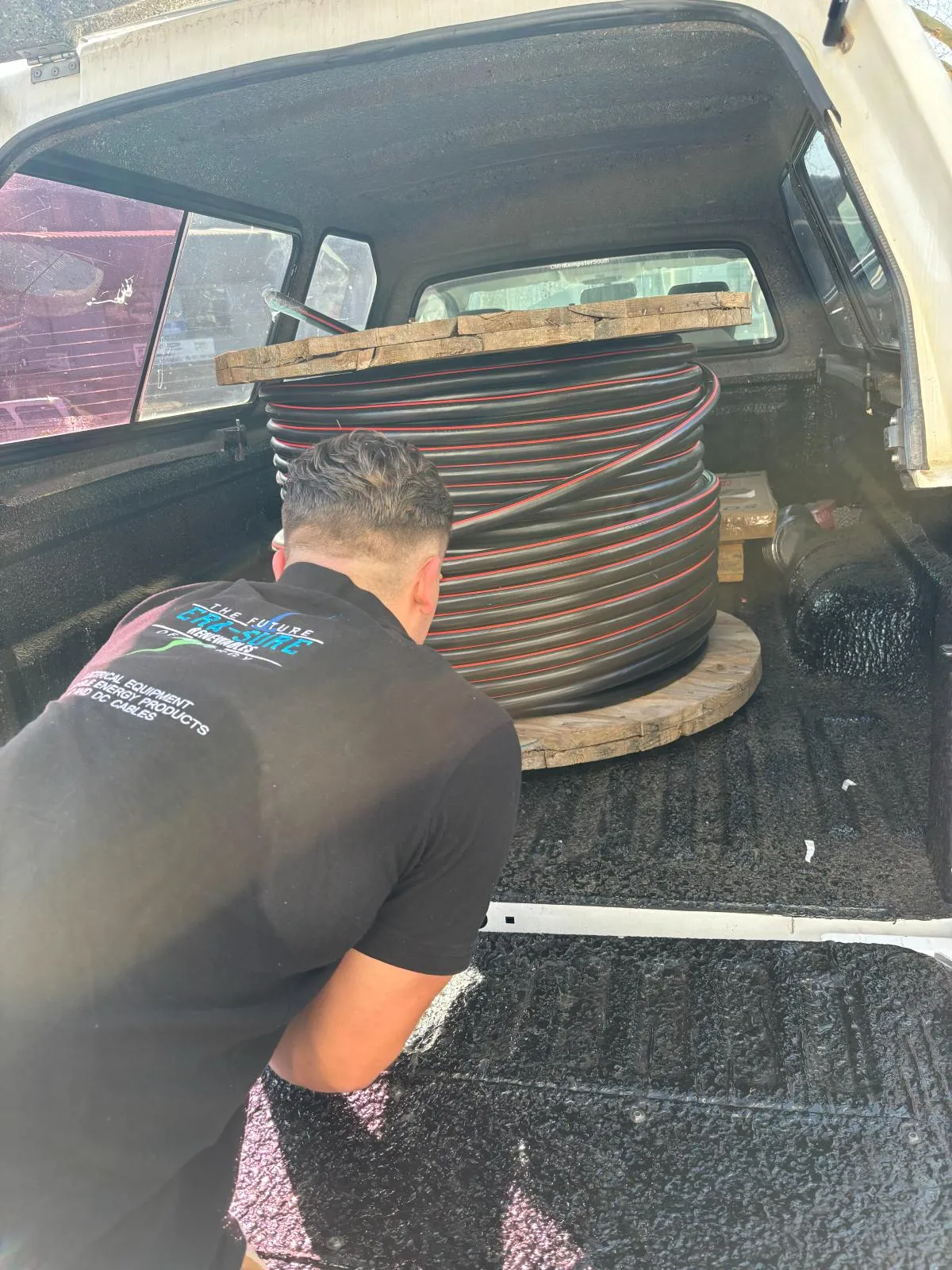 A member of the Era-Sure team securing a drum of red and black cable in a vehicle load bed.