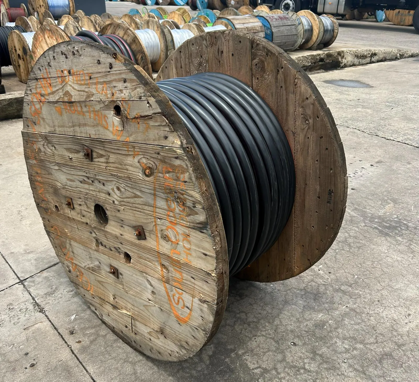 A large drum of black cable in a yard lined with further cable drums.