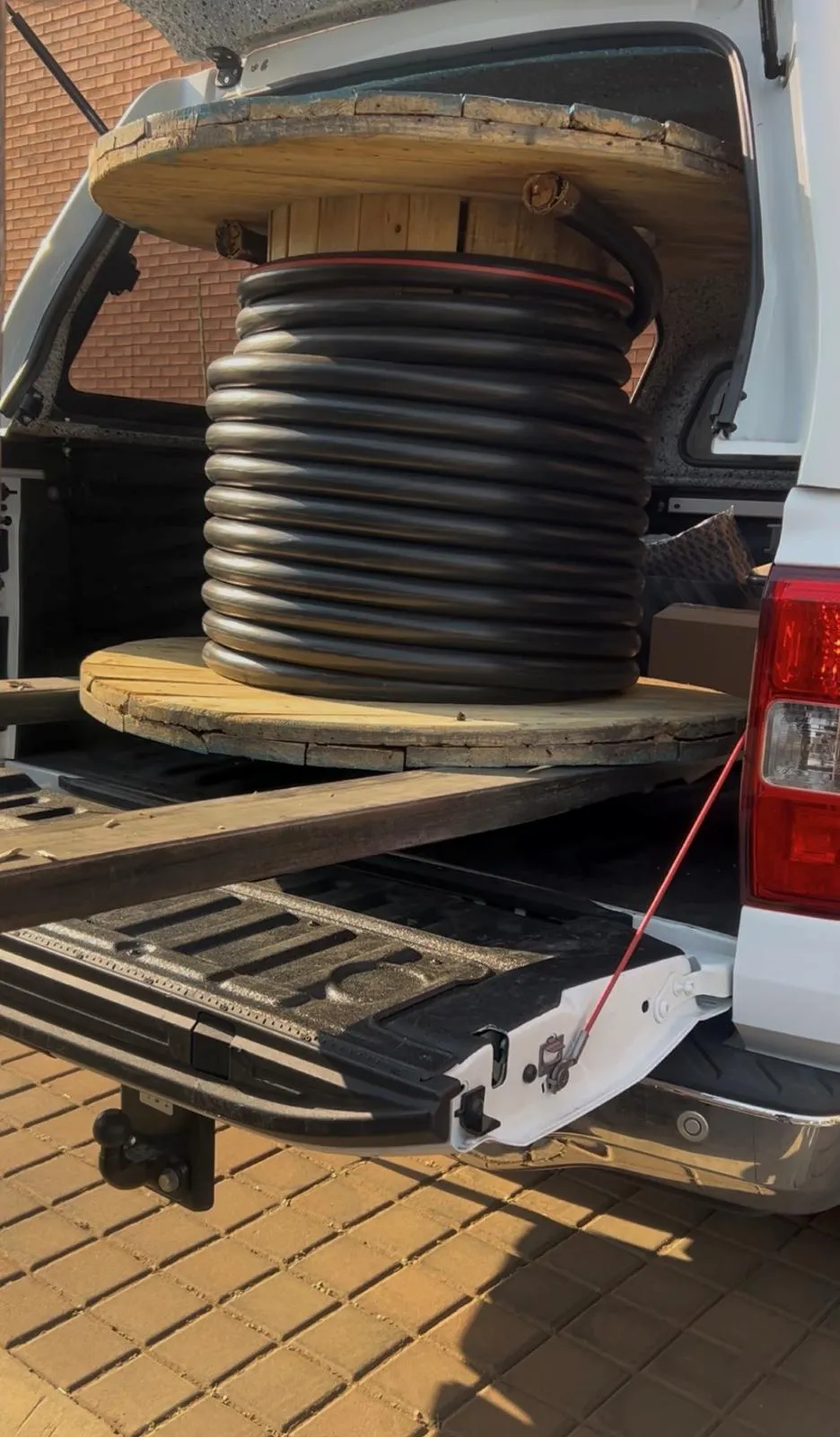 A drum of heavy black cable secured on an open vehicle tailgate.