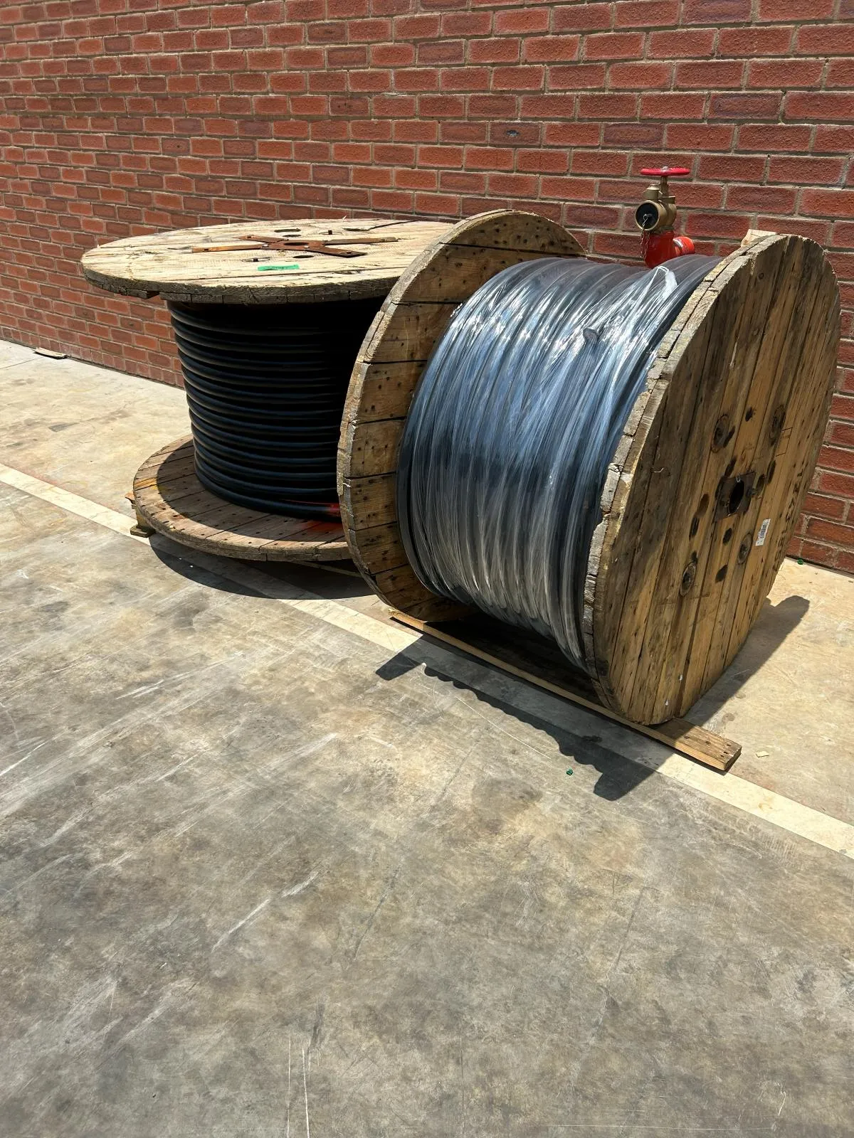 Two large cable drums standing side by side against a brick wall.