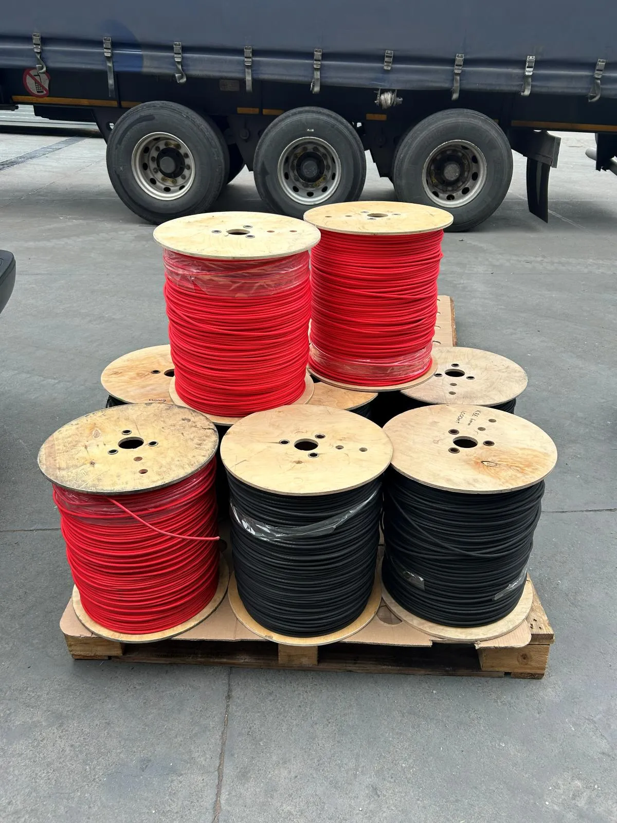 Red and black cable reels stacked on a pallet beside a delivery truck.