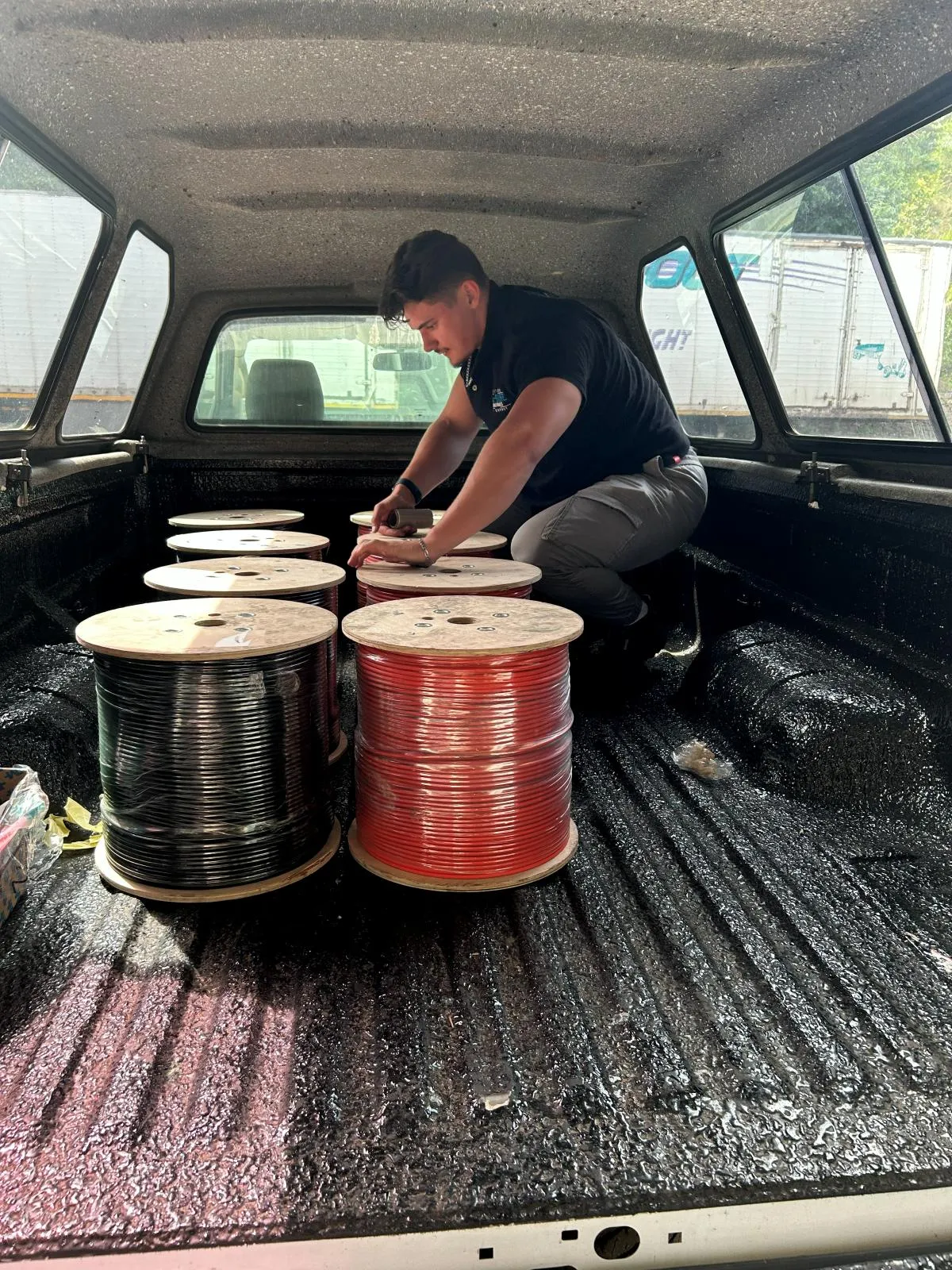 A member of the Era-Sure team securing black and red cable reels in a vehicle load bed.