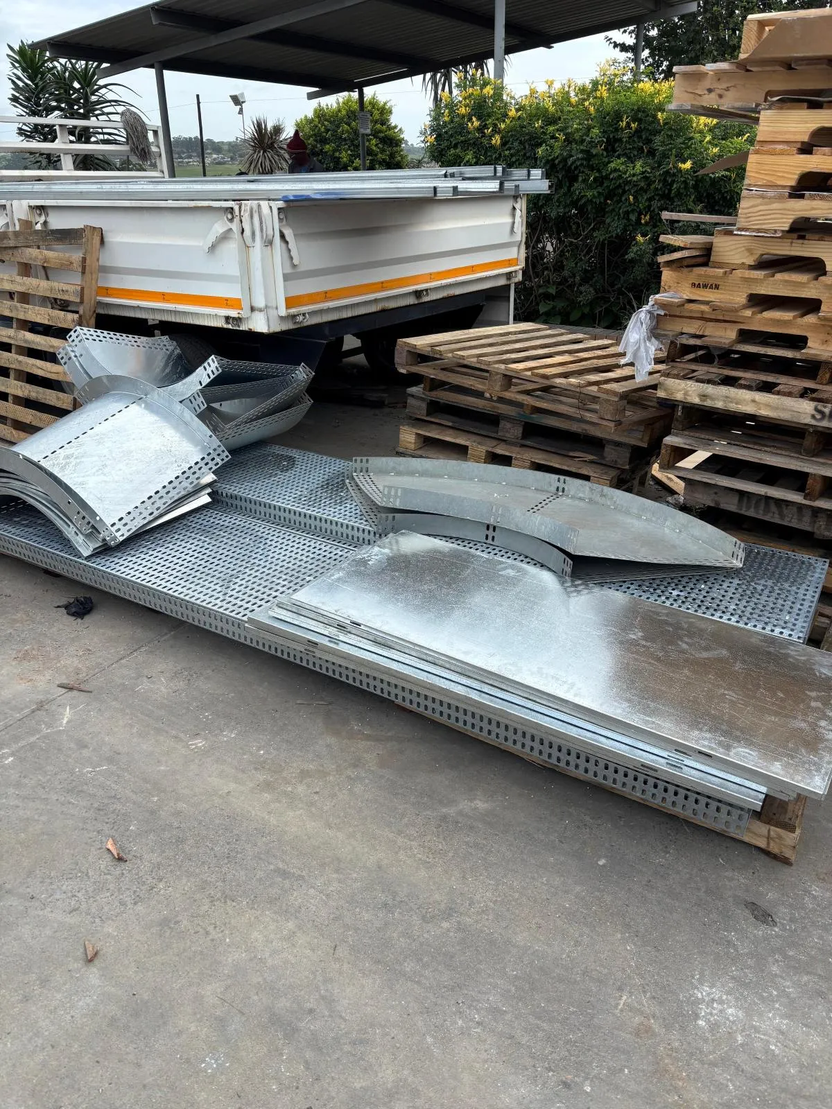 Wide perforated cable trays with flat covers and curved bends stacked beside a vehicle load bed.