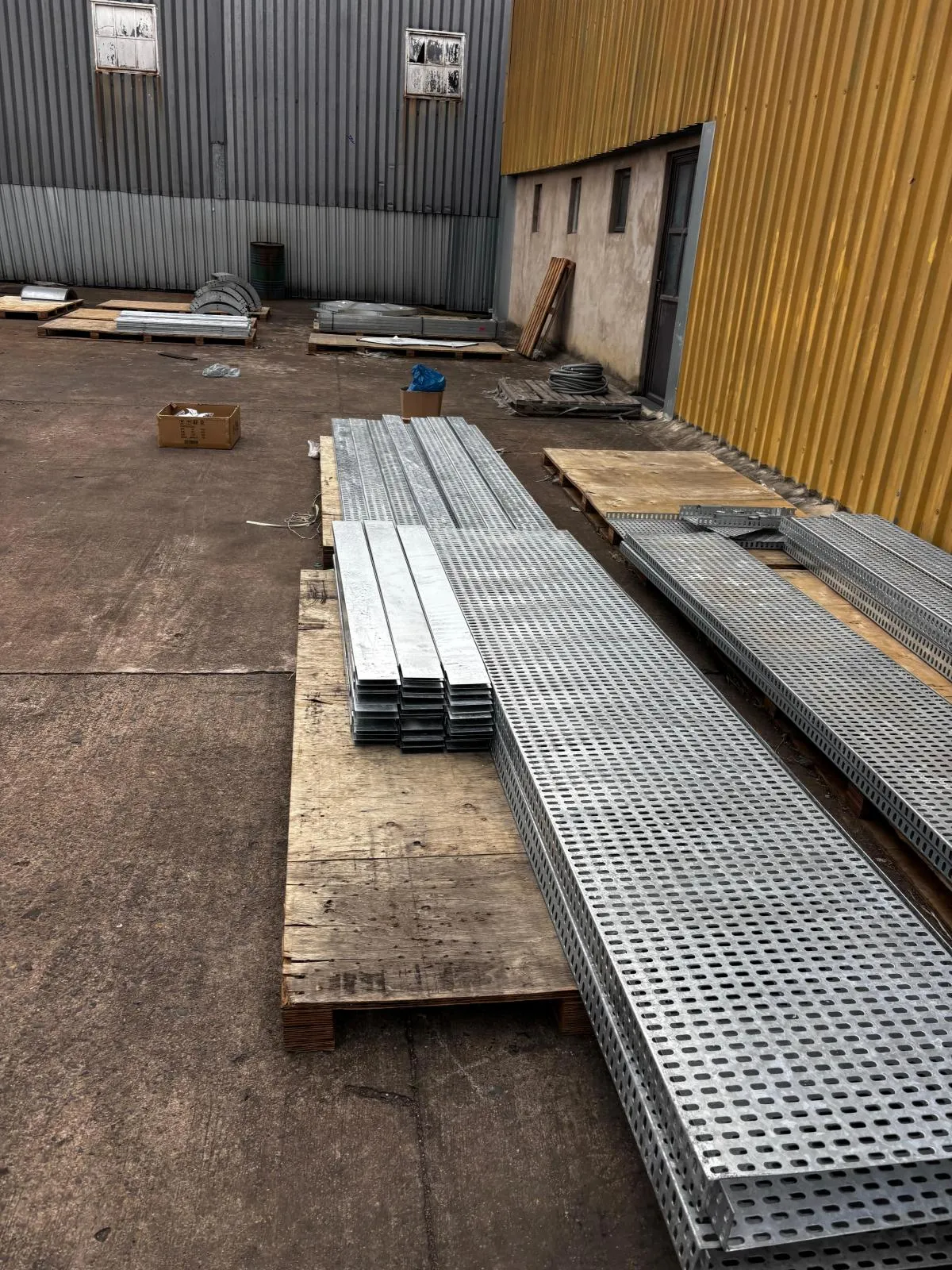 Long lengths of perforated cable tray and channel stacked on timber pallets in a supplier yard.