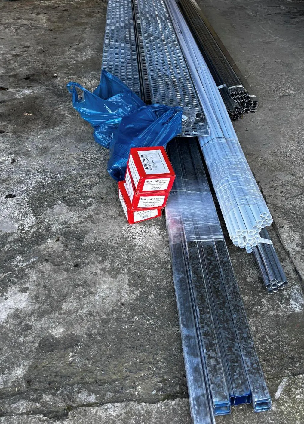 Perforated cable tray, steel trunking, white PVC conduit and boxed cable glands laid out on a warehouse floor.