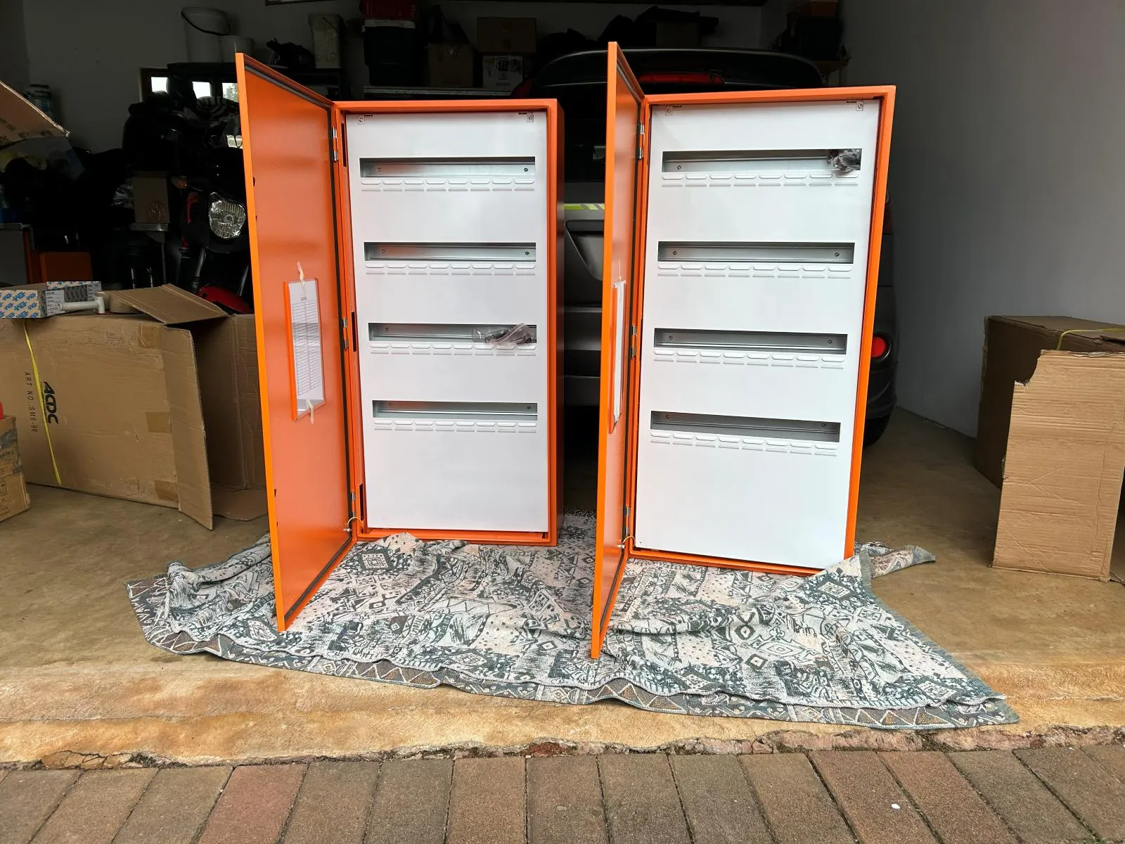 Two orange enclosures with white distribution boards mounted inside and their doors open.