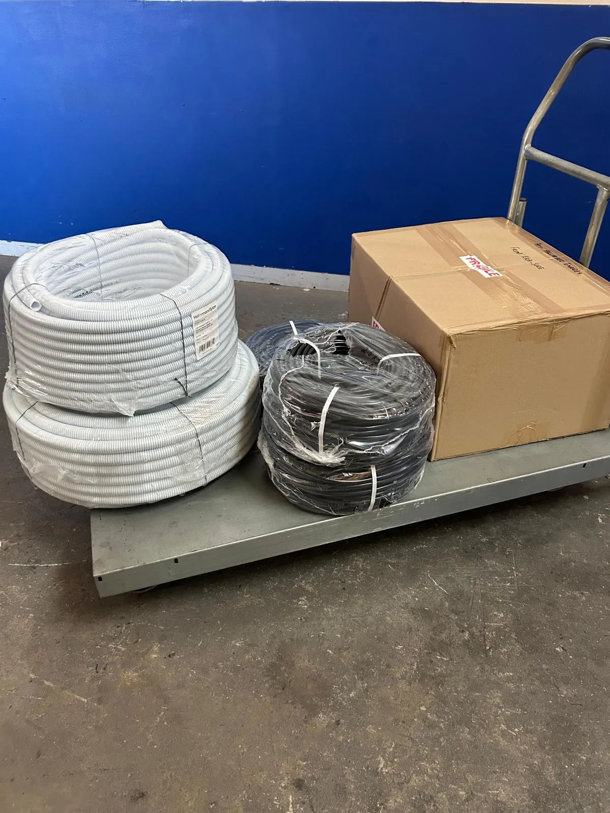 Coils of white flexible conduit and black cable beside a boxed order on a trolley