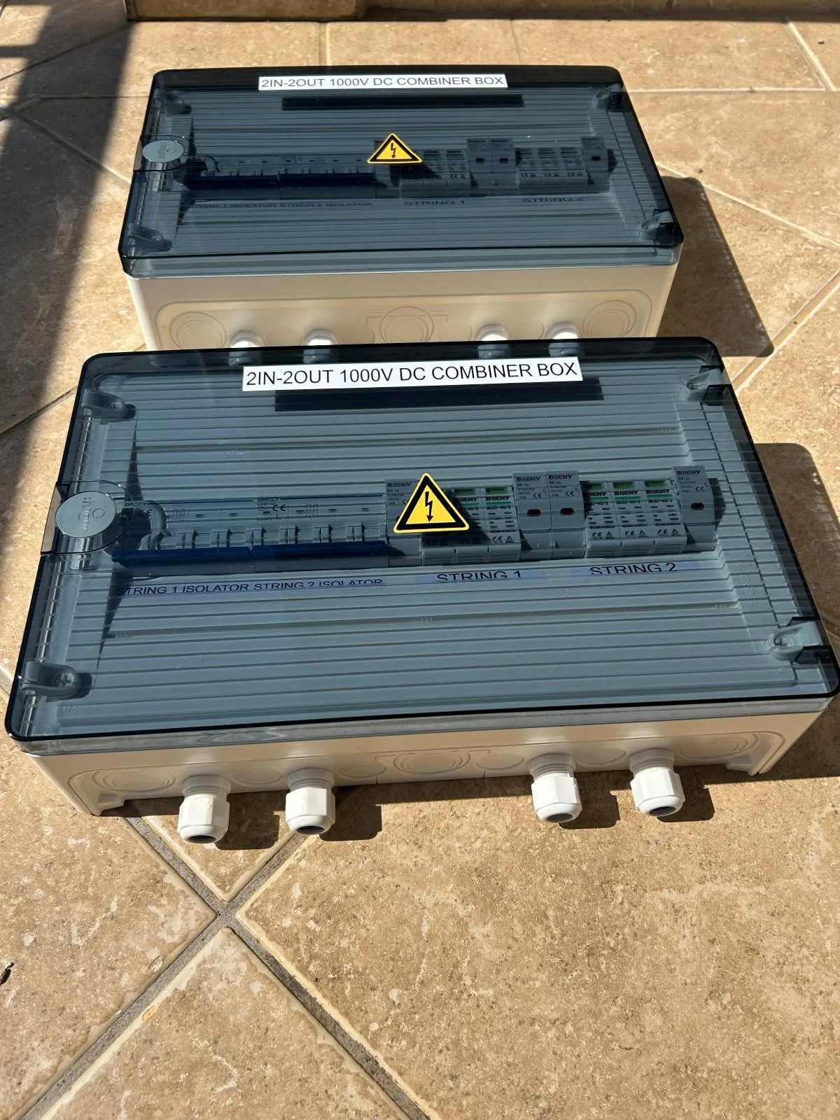 Two 1000 volt DC combiner boxes with smoked covers, warning labels and cable glands along the base.
