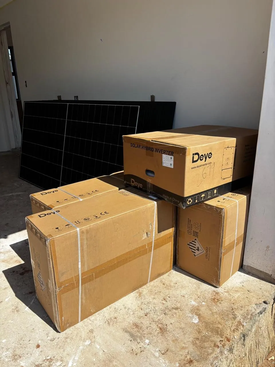 A boxed Deye hybrid inverter and battery packs grouped beside a solar panel