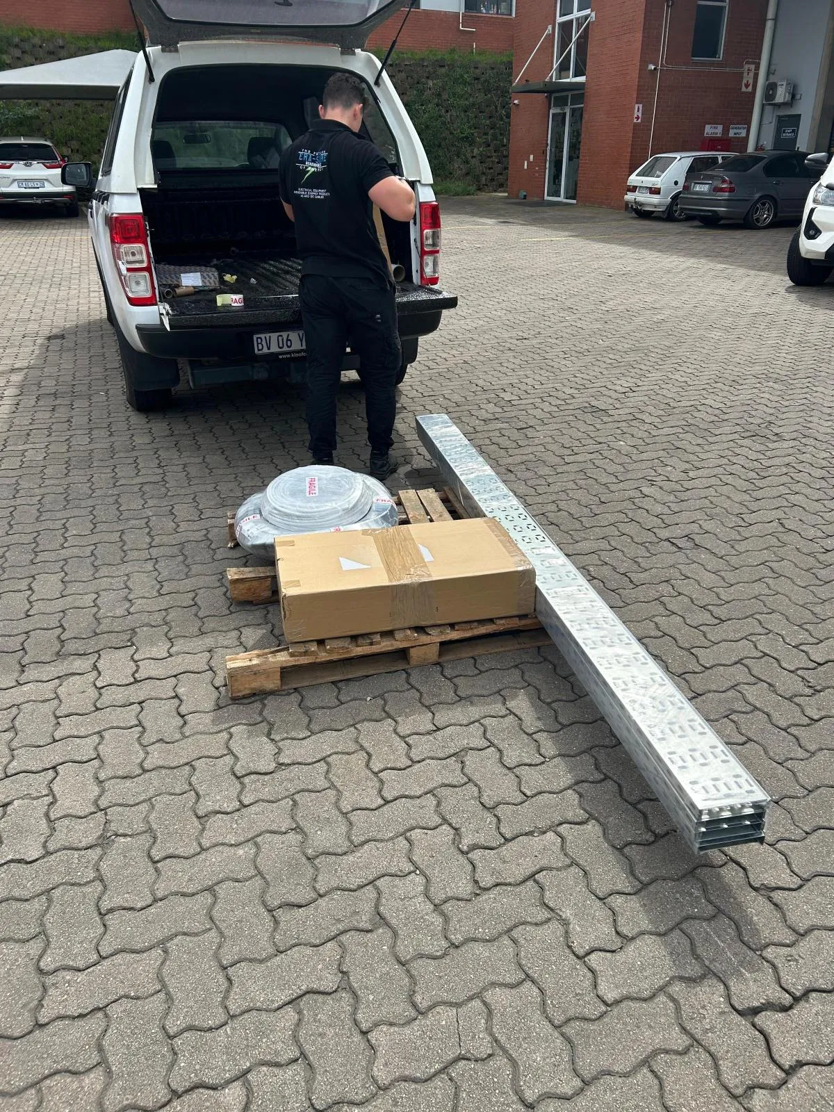 An Era-Sure team member beside a pallet of coiled conduit, boxed accessories and cable trays at a vehicle load bed