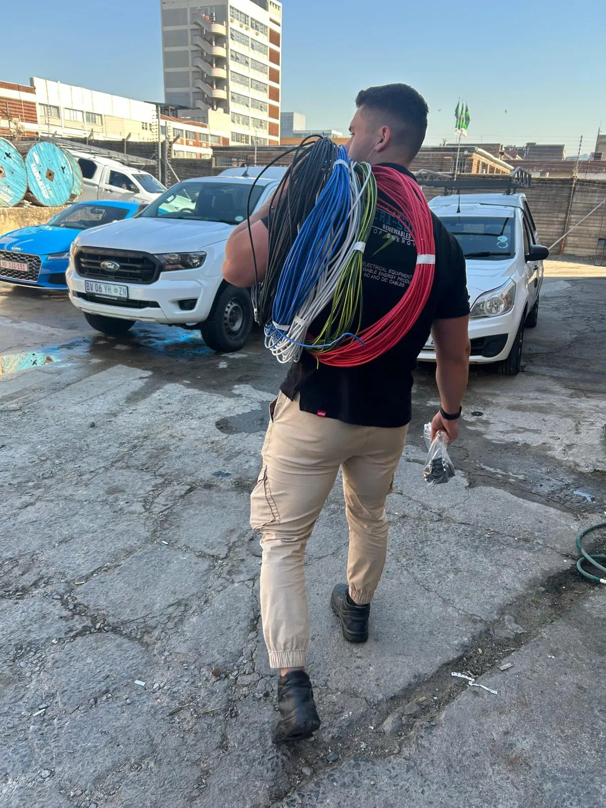 An Era-Sure team member carrying coils of coloured electrical wire across a yard