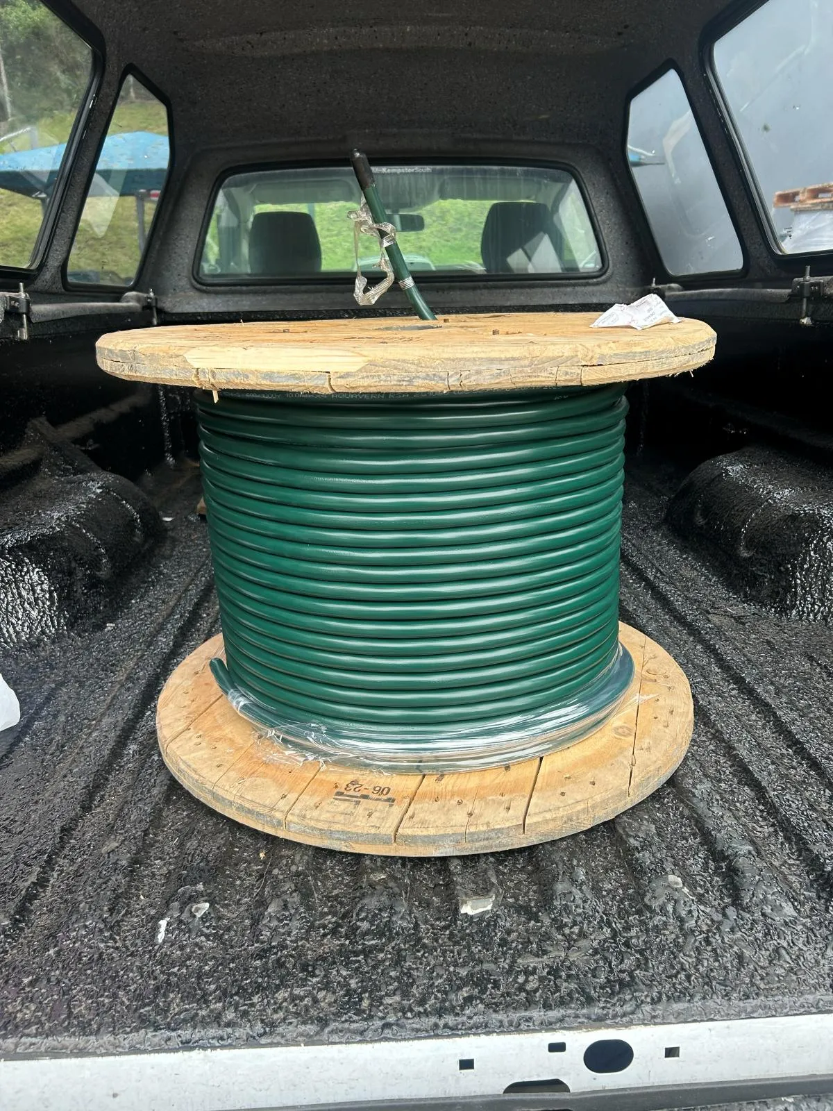 A reel of green cable loaded in a vehicle load bed.