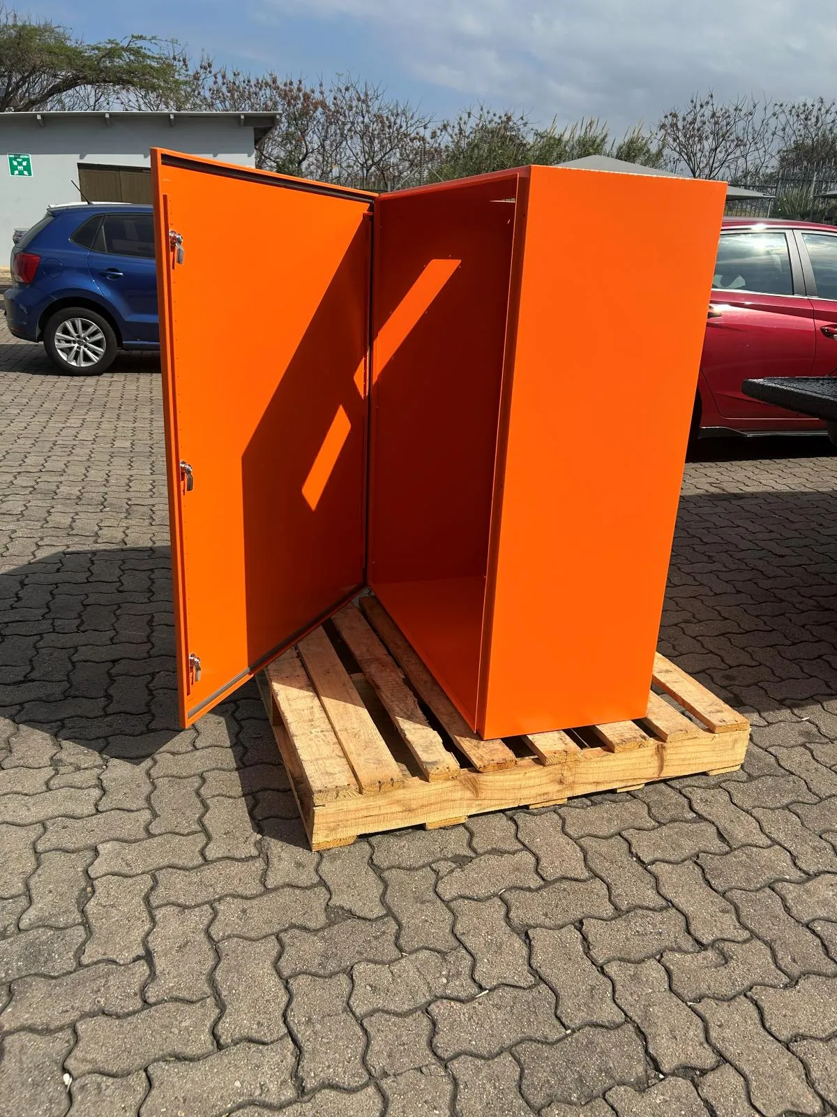 A tall orange steel enclosure standing on a pallet with both doors open.
