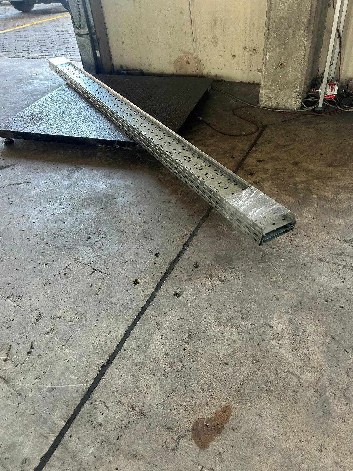 A single length of perforated galvanised cable tray resting across a workshop floor.