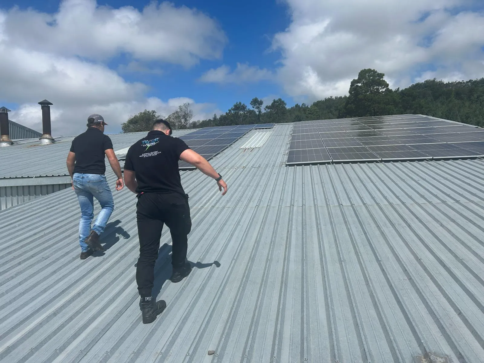 Two Era-Sure team members crossing a corrugated roof towards a mounted array of solar panels