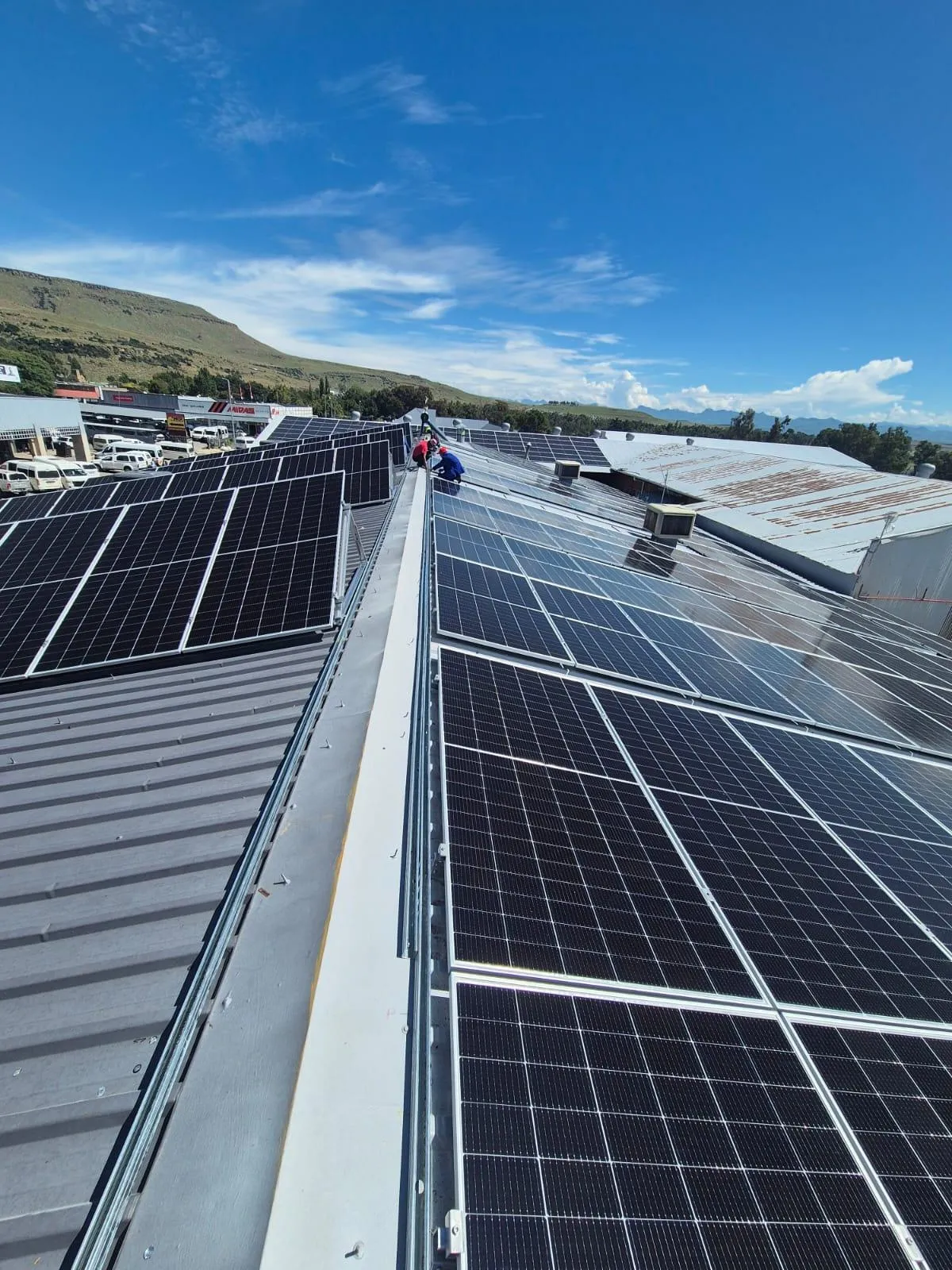 Long rows of solar panels mounted across two adjoining industrial roofs under a clear sky