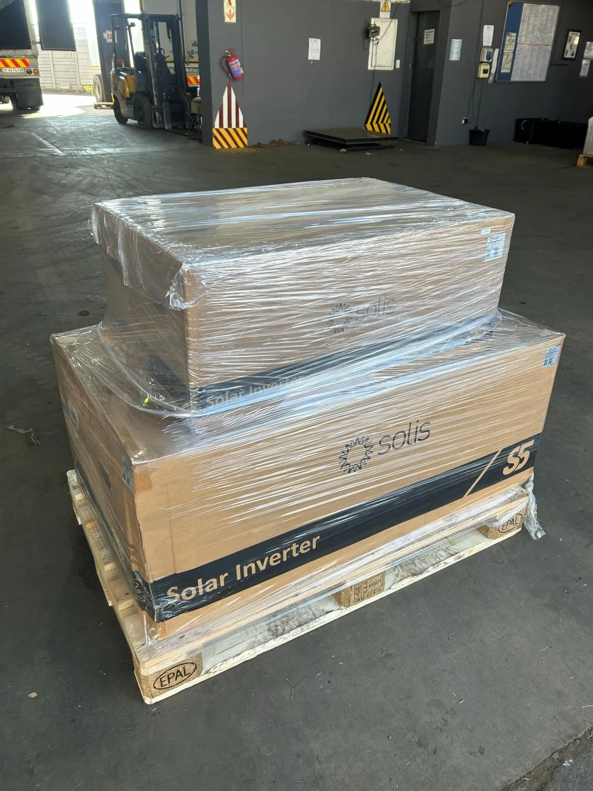 Two boxed Solis S5 solar inverters shrink-wrapped on a wooden pallet in a warehouse