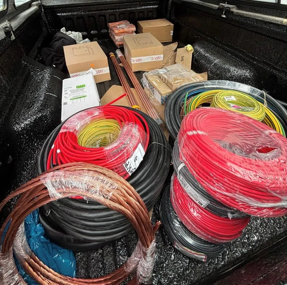 A vehicle load bed filled with boxed switchgear, coils of solar cable and bare copper earth conductor