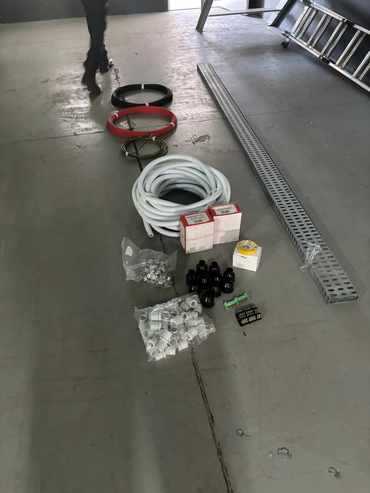 Cable coils, flexible conduit, glands, terminal blocks and a length of cable tray laid out on a workshop floor