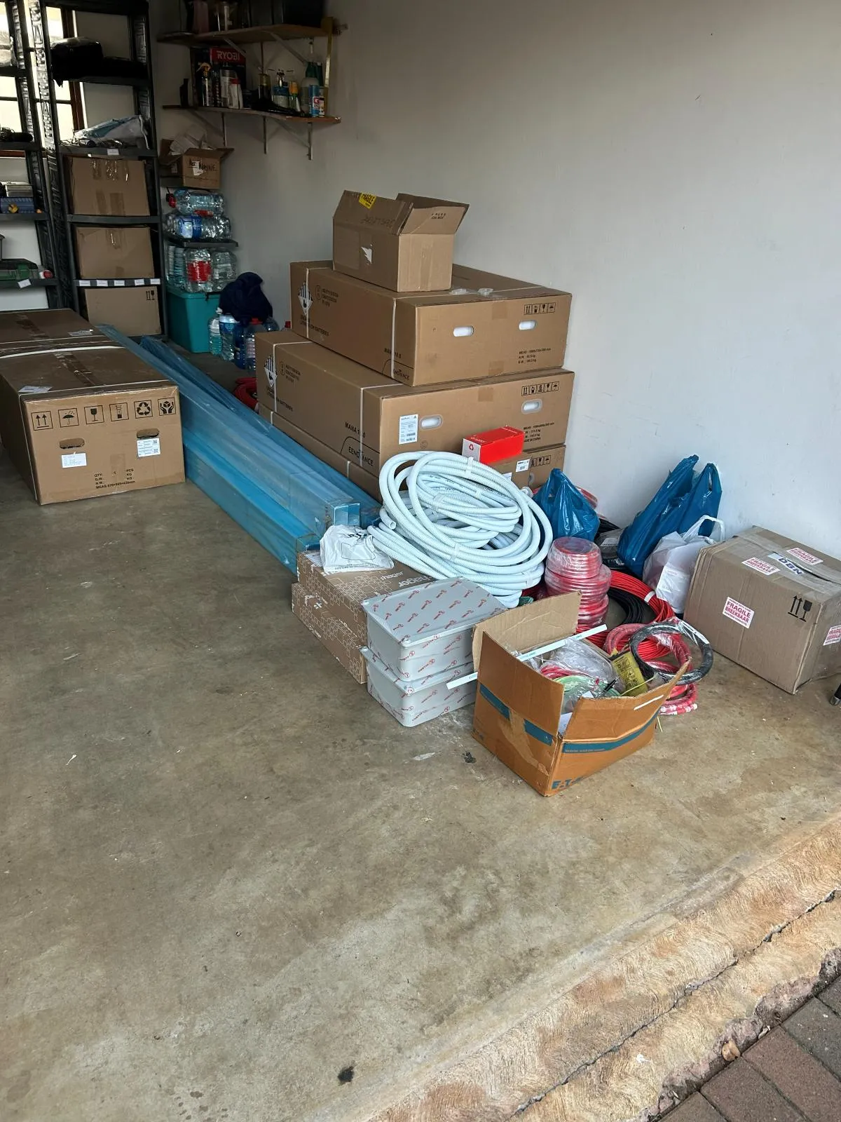 Boxed batteries, enclosures, coiled conduit and cartons marked fragile switchgear staged against a wall